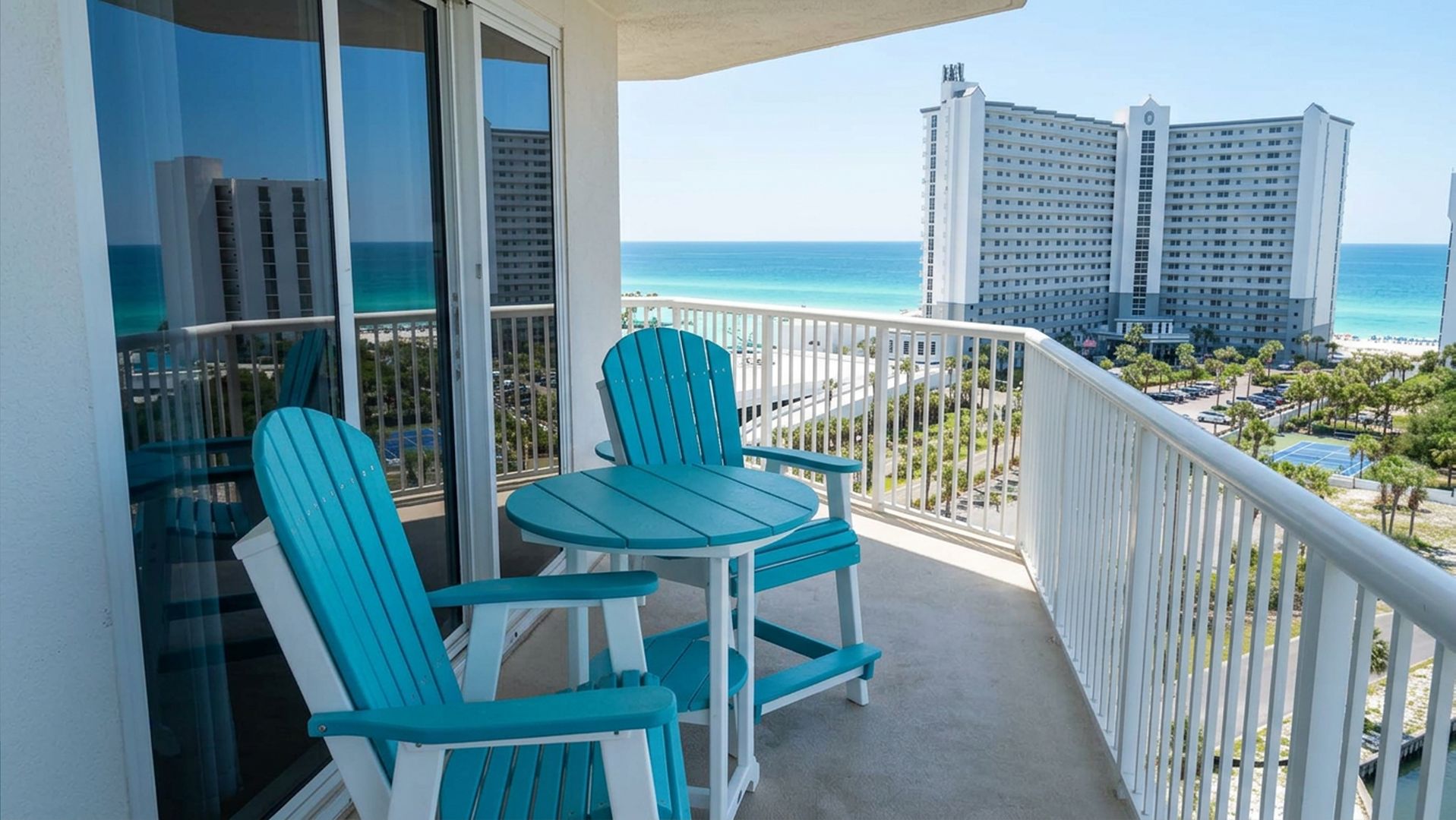 Un balcone con due sedie e un tavolo, vista sulla spiaggia e palazzi alti.