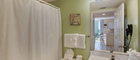 Un baño con cortina de ducha, inodoro con toallero, lavabo con espejo y un cartel en la pared.