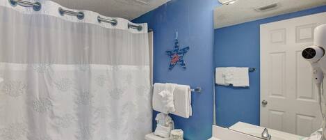 A bathroom with a white shower curtain, a blue wall, a white toilet, a white sink with a mirror, and a hairdryer.