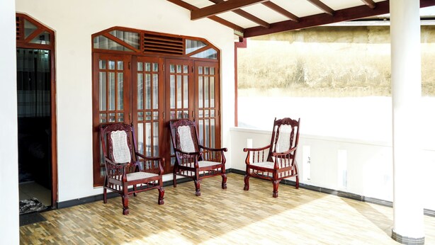 Une pièce avec trois chaises en bois, une porte en bois dotée de panneaux de verre et un plafond blanc avec des poutres en bois.
