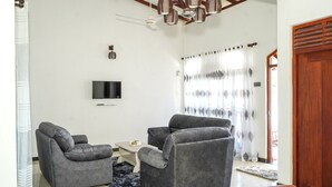 Un salon avec deux canapés gris, une petite table blanche, un téléviseur fixé au mur et une porte en bois.