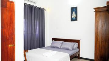A neatly made bed with a white bedspread and two pillows, a wooden headboard, a gray curtain, and a framed picture on the wall.