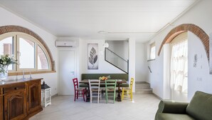 Amplia sala de estar con una mesa de comedor, sillas coloridas, un sofá verde y una escalera que sube a otro nivel.