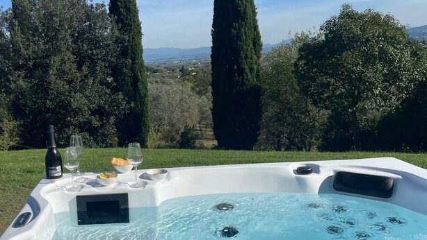 Un jacuzzi con una mesa para dos, con vistas a un paisaje pintoresco con árboles y colinas.