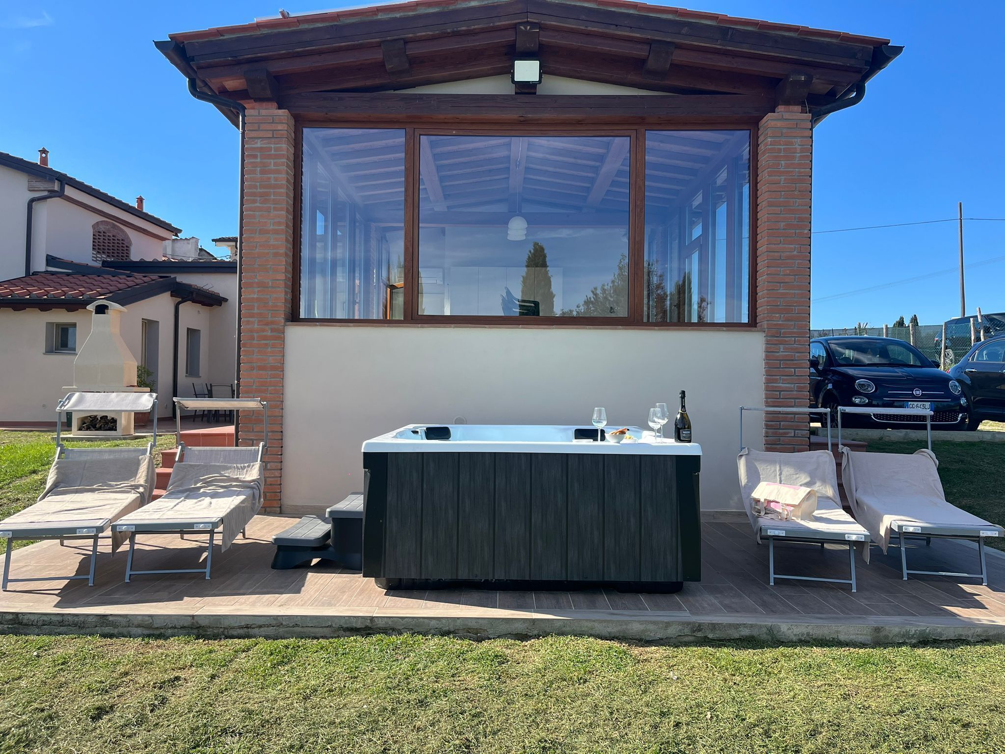 A covered outdoor hot tub area with lounge chairs, a table, and a grill.