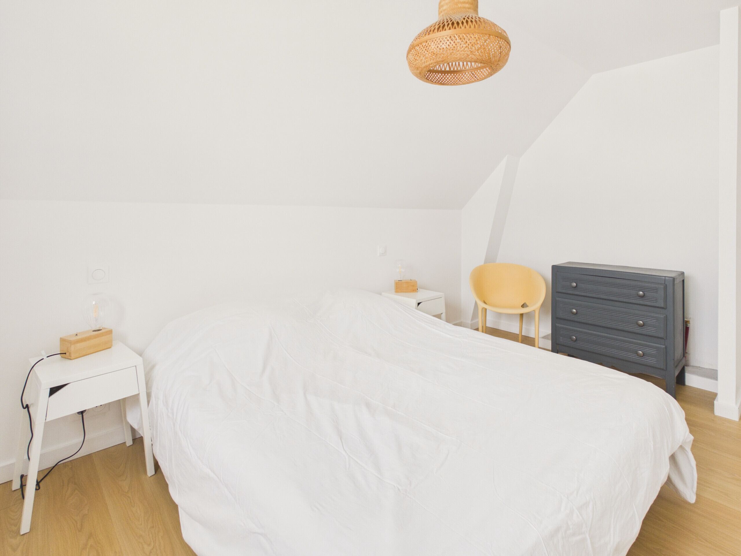 A bedroom with a bed, a nightstand, a chair, a dresser, and a hanging light fixture.