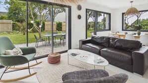 A modern living room with a glass door leading to a garden, a leather sofa, a rocking chair, and a coffee table. - 490m from the beach, new house for 8 (Trégunc)