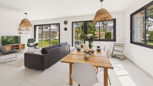 A modern living space with a sofa, dining table, and chairs, large windows, and a TV. - 490m from the beach, new house for 8 (Trégunc)