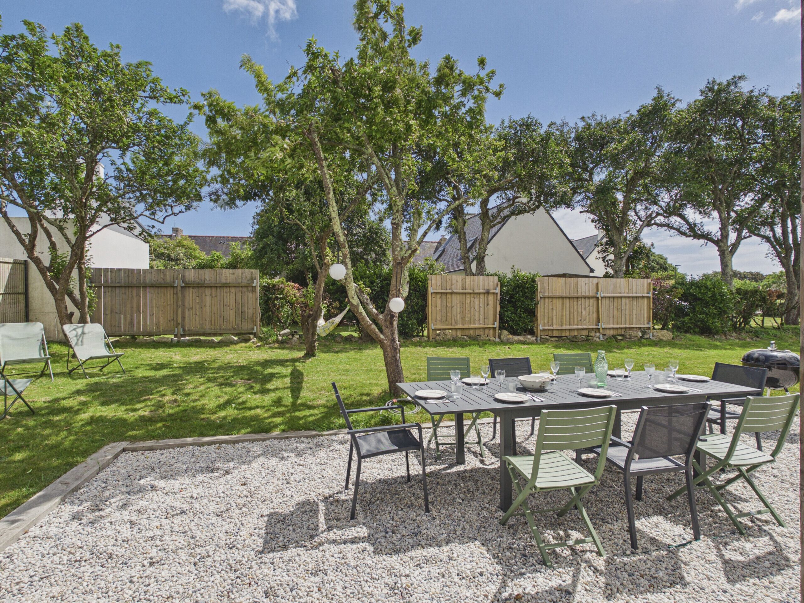 An outdoor patio with a table set for dining, surrounded by chairs, and a barbecue grill in the background.
