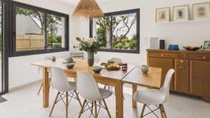 A modern dining area with a wooden table, white chairs, a vase with flowers, and a hanging light fixture. - 490m from the beach, new house for 8 (Trégunc)