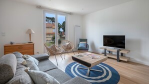 Un salon moderne comprenant un canapé, des fauteuils, une table basse, un téléviseur et une porte-fenêtre coulissante donnant sur un balcon.
