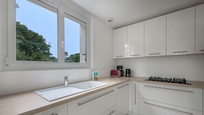 Une cuisine moderne avec des meubles blancs, un évier double et une fenêtre donnant sur les arbres.
