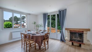 Un coin repas avec une table dressée pour quatre personnes, une cheminée et de grandes fenêtres avec des rideaux.