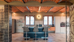 Een moderne keuken met een bakstenen plafond, een centraal kookeiland met barstoelen, een wijnkoeler en inbouwapparatuur.