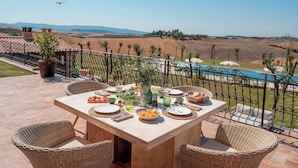 Een terras met een eettafel, met uitzicht op een zwembad en glooiende heuvels.