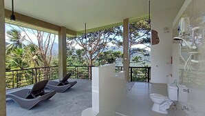 A bathroom with a toilet, shower, and a balcony with two lounge chairs.