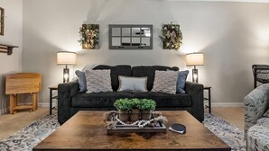 Een woonkamer met een donkergrijze bank, twee bijzettafels met lampen, een houten salontafel met decoratieve objecten, en kamerbreed tapijt.