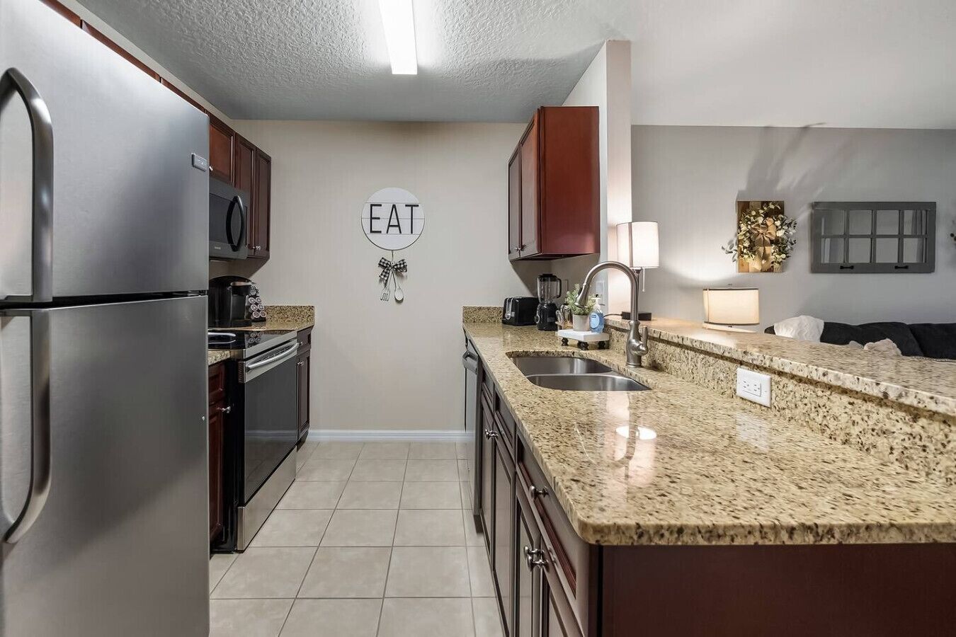 A modern kitchen with stainless steel appliances, a granite countertop, and a 'EAT' sign on the wall.