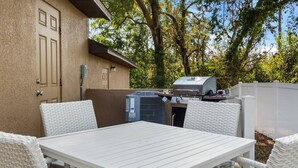 Een terras met een witte tafel en stoelen, een barbecue en een airconditioning.