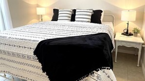 Een slaapkamer met een bed, twee nachtkastjes, een wandklok en een bordje met de tekst 'STAY awhile'.