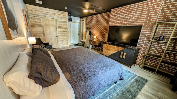 A modern bedroom with a large bed, a TV, and a brick wall. - Casa Bonita - A mid-century retreat in Grand Junction! (Grand Junction)