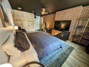 A modern bedroom with a large bed, a TV, and a brick wall.