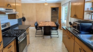 A modern kitchen with wooden cabinets, a gas stove, a microwave, and a dining table with chairs. - Casa Bonita - A mid-century retreat in Grand Junction! (Grand Junction)
