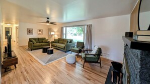 A spacious living room with a wooden floor, green sofas, a round coffee table, and a fireplace. - Casa Bonita - A mid-century retreat in Grand Junction! (Grand Junction)