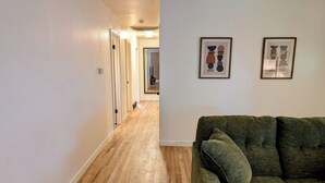 A hallway with wooden flooring leading to a room with a green sofa and two framed artworks on the wall. - Casa Bonita - A mid-century retreat in Grand Junction! (Grand Junction)