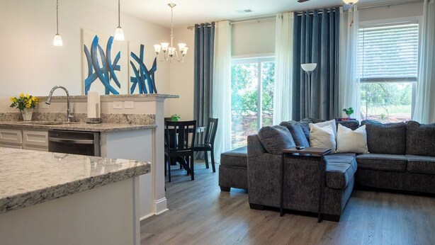 A modern kitchen with granite countertops, a dining area with a table and chairs, and a living room with a gray sectional sofa. - Feels Like Home! Columbia near Fort Jackson - Perfect for Families - Sleeps 6 (Elgin)