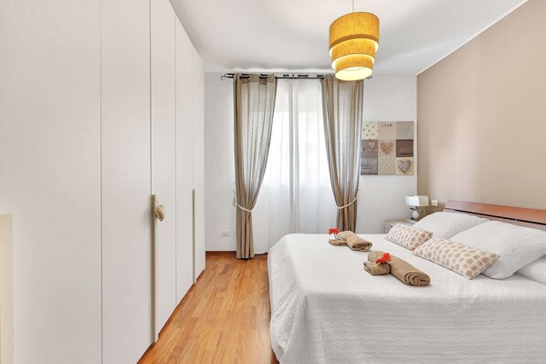 Una cama bien hecha con toallas enrolladas y almohadas, un suelo de madera, una lámpara colgante y un cuadro en la pared.
