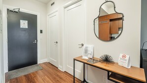 A hallway with a wooden floor, a desk with a mirror, and a door with a sign.