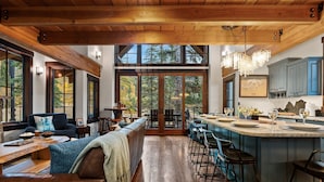 Amplia sala de estar con un gran techo de madera, un rincón de descanso acogedor y una cocina con alacenas azules y una barra.