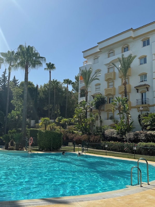 Una piscina rodeada de palmeras y un edificio con balcones.