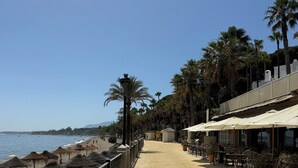 Un paseo marítimo con una playa a un lado y una fila de asientos y sombrillas al aire libre al otro.