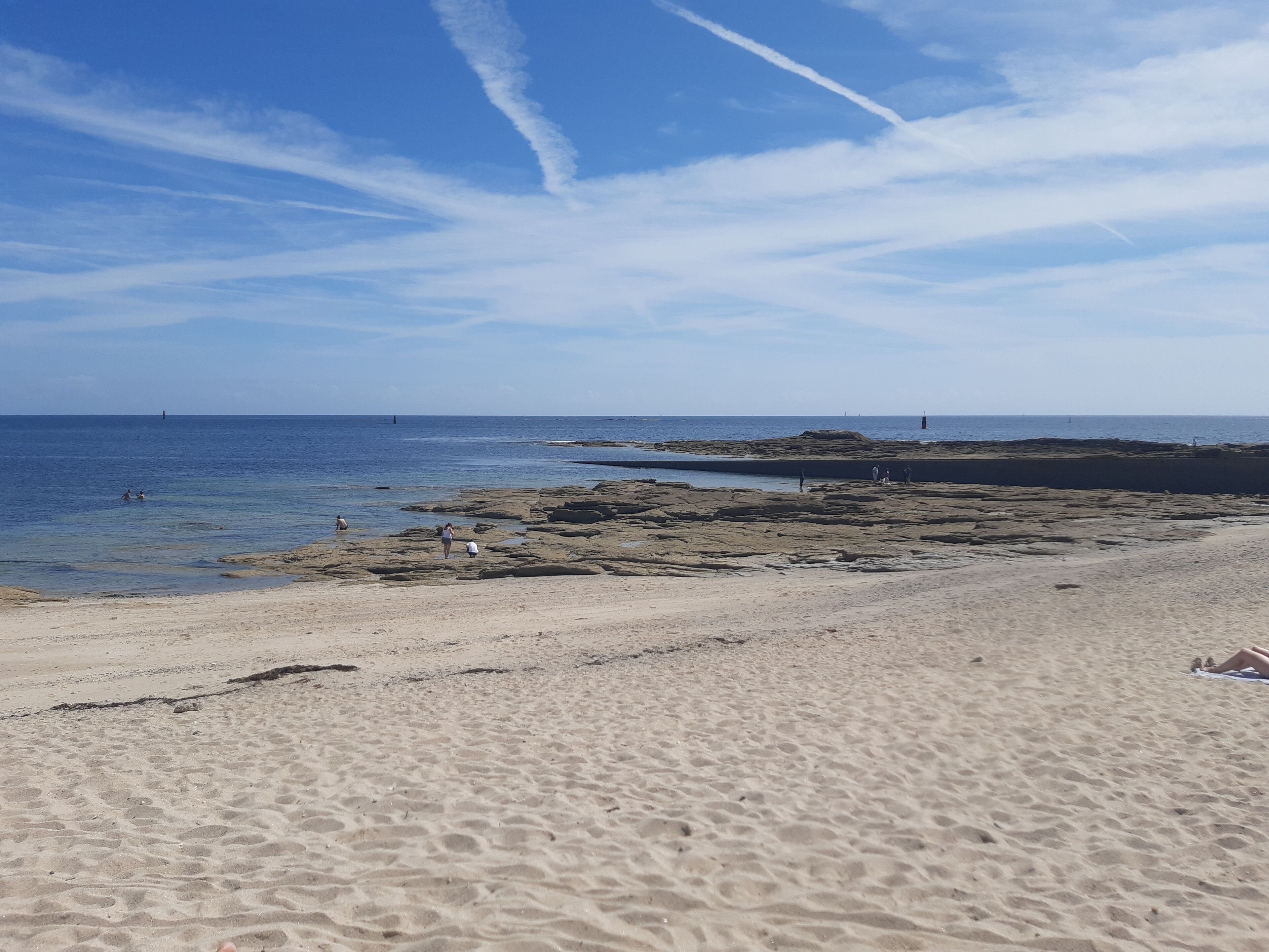 A sandy beach with rocky outcrops and a clear blue sky.
