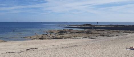 A sandy beach with rocky outcrops and a clear blue sky.