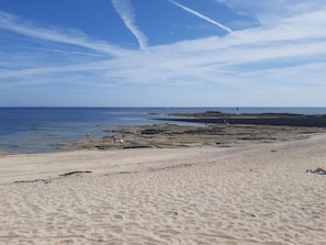 Una spiaggia sabbiosa con affioramenti rocciosi e un cielo azzurro limpido.