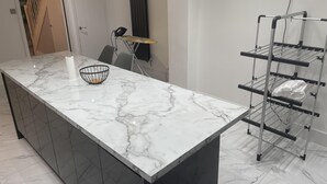 Μια μοντέρνα κουζίνα με πάγκο από μάρμαρο, ένα μαύρο μεταλλικό καλάθι και μια μεταλλική στεγνωτήρα.