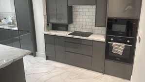 Μια μοντέρνα κουζίνα με σκούρα ντουλάπια, έναν φούρνο Bosch και έναν πάγκο από μάρμαρο.