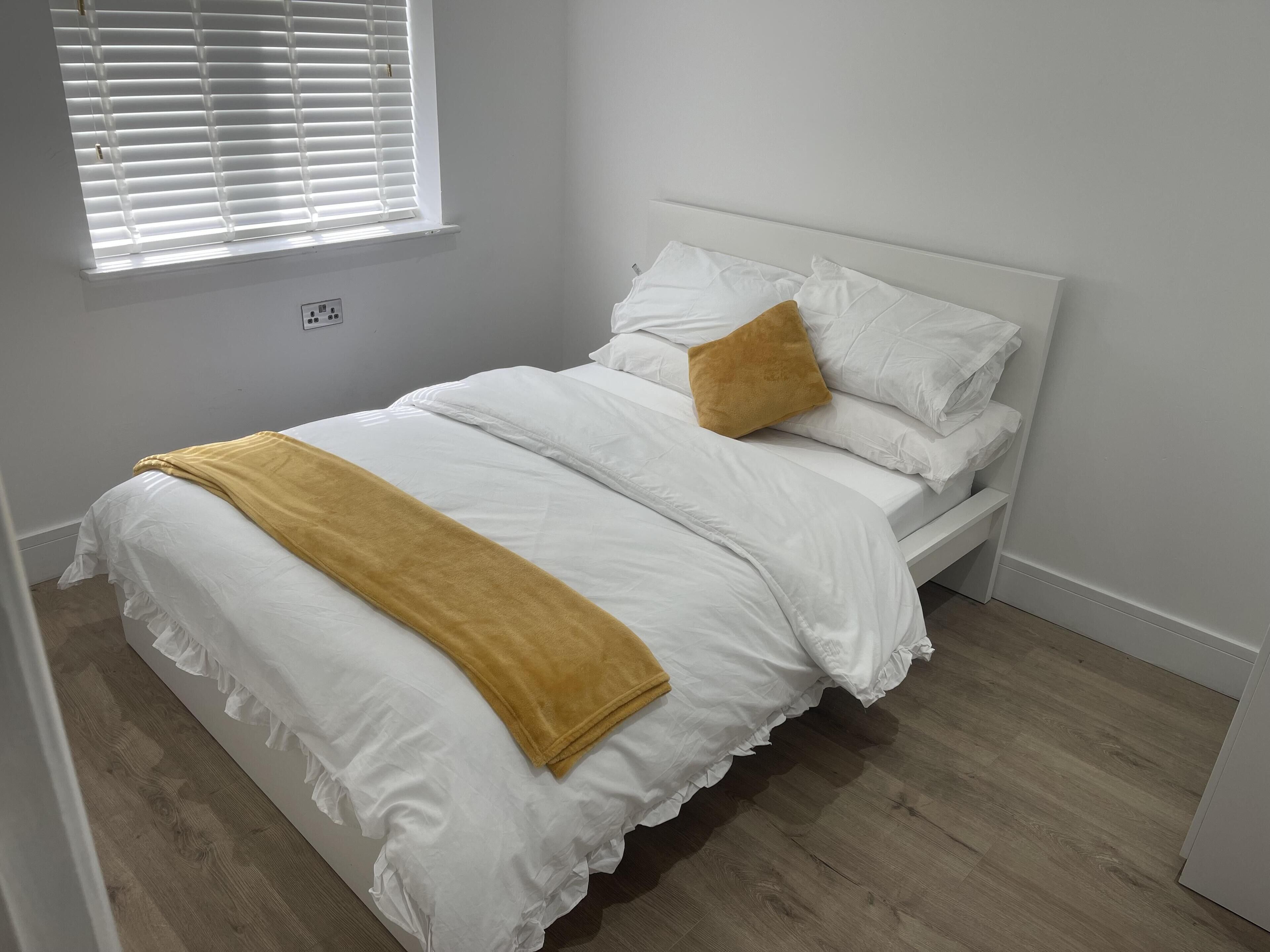 A neatly made bed with white bedding and a mustard-colored throw blanket, a single mustard-colored pillow, and a white headboard.