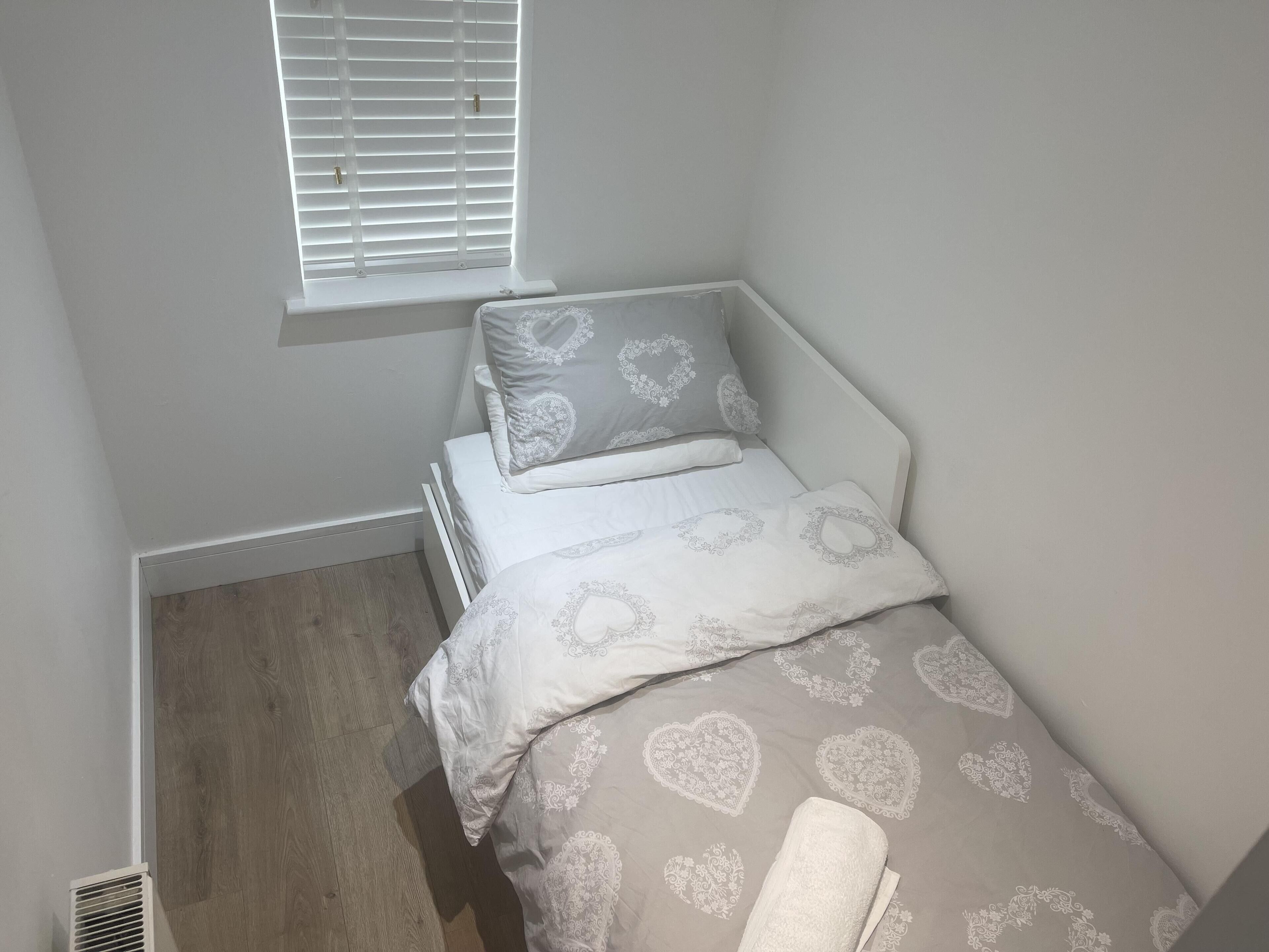 Ein kleines Zimmer mit einem Einzelbett, einem Fenster, weißen Wänden und einem Holzboden.