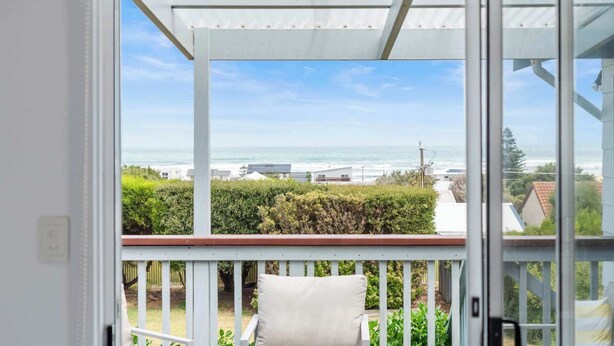 Een balkon met een witte reling, een kussen en uitzicht op de oceaan en gebouwen.