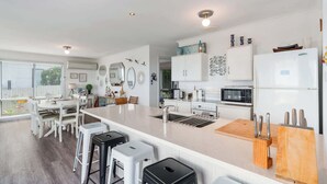 Een moderne keuken met witte kasten, een centraal eiland, barkrukken, een magnetron en een koelkast.