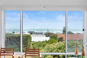 A room with a large window overlooking a coastal view, two wooden chairs, and a small table with decorative items.