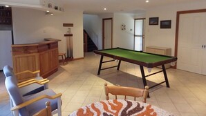 A room with a pool table, a bar area, and a staircase leading to another level.