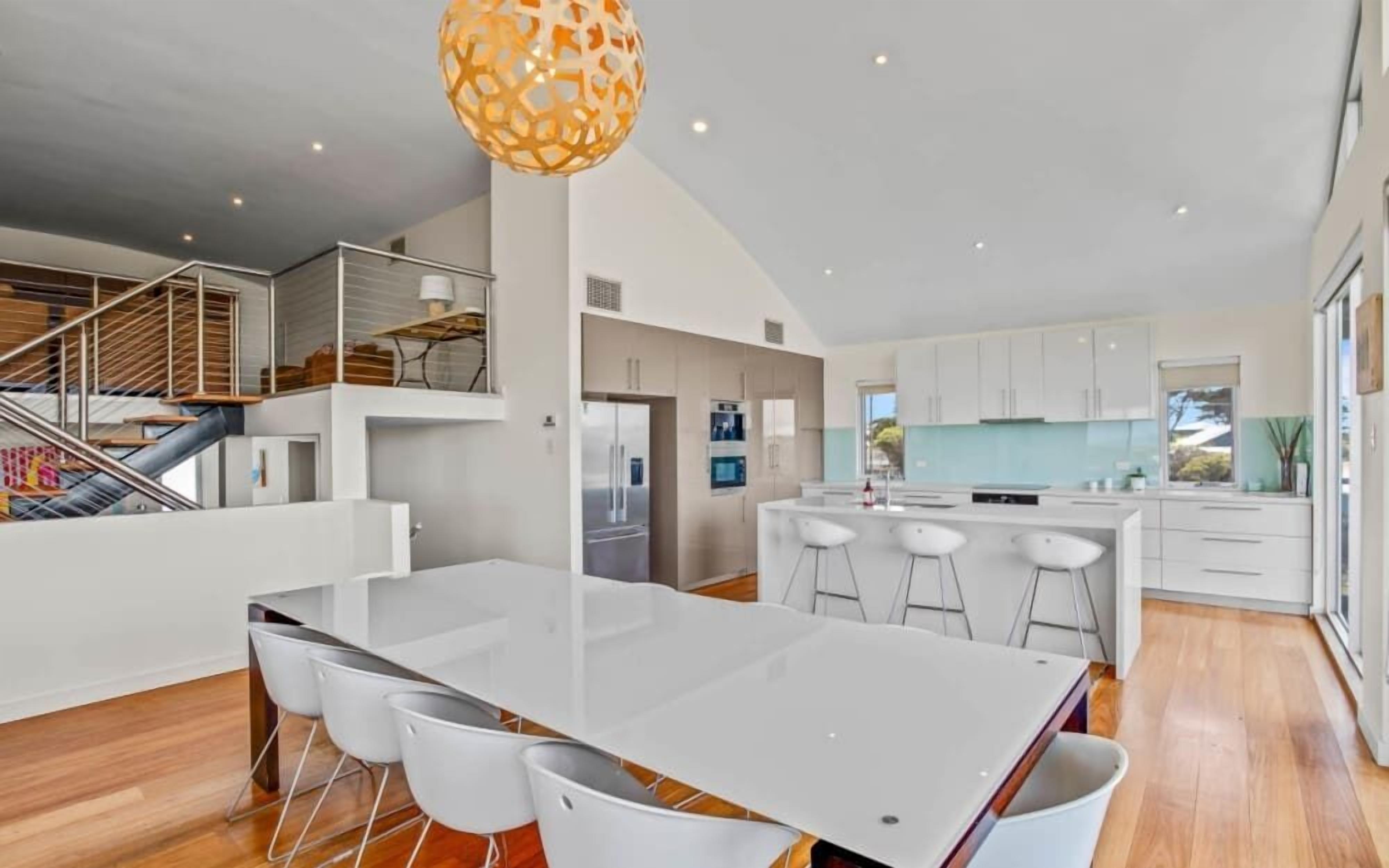 A modern kitchen with white cabinets, a central island with bar stools, and a staircase leading to an upper level.
