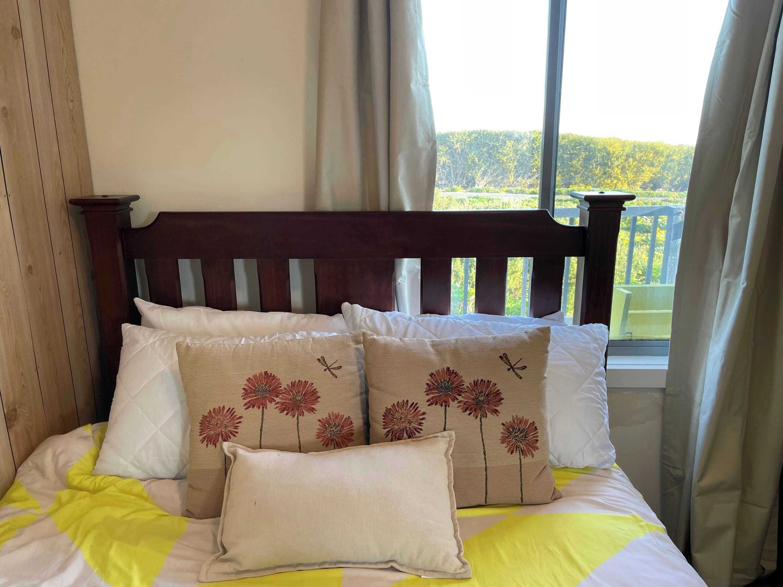 Una cama con cabecera de madera, varios almohadones y vistas a la vegetación a través de una ventana.