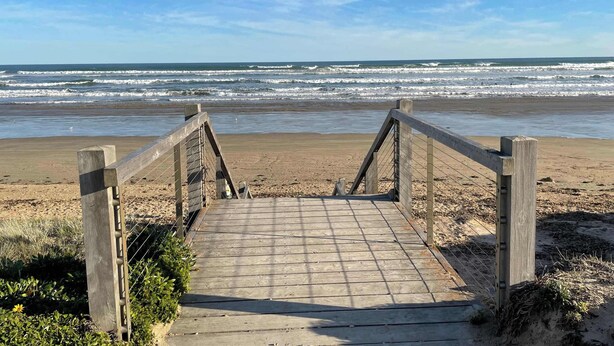 Une promenade en bois menant à une plage, avec des vagues en arrière-plan.