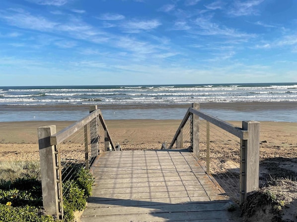 A wooden boardwalk leading to a beach with waves in the background.